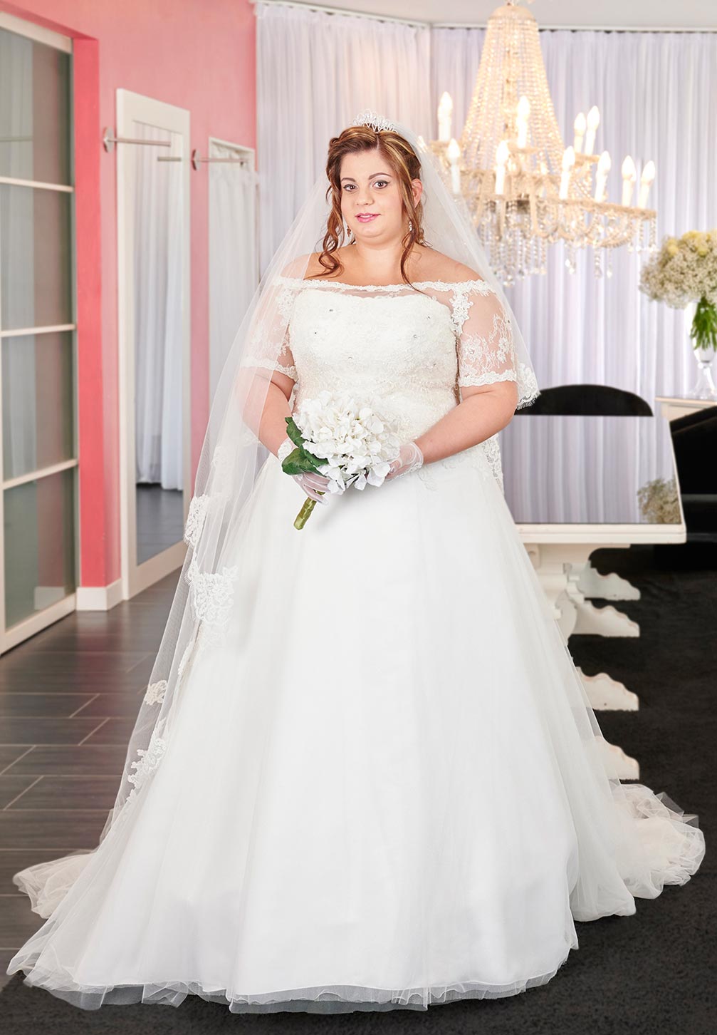 Abito da sposa curvy. Abito intero romantico dal sapore regale e sofisticato, a redingote in morbido pizzo dai delicati toni ecrù con scollo totale con applicazioni floreali.